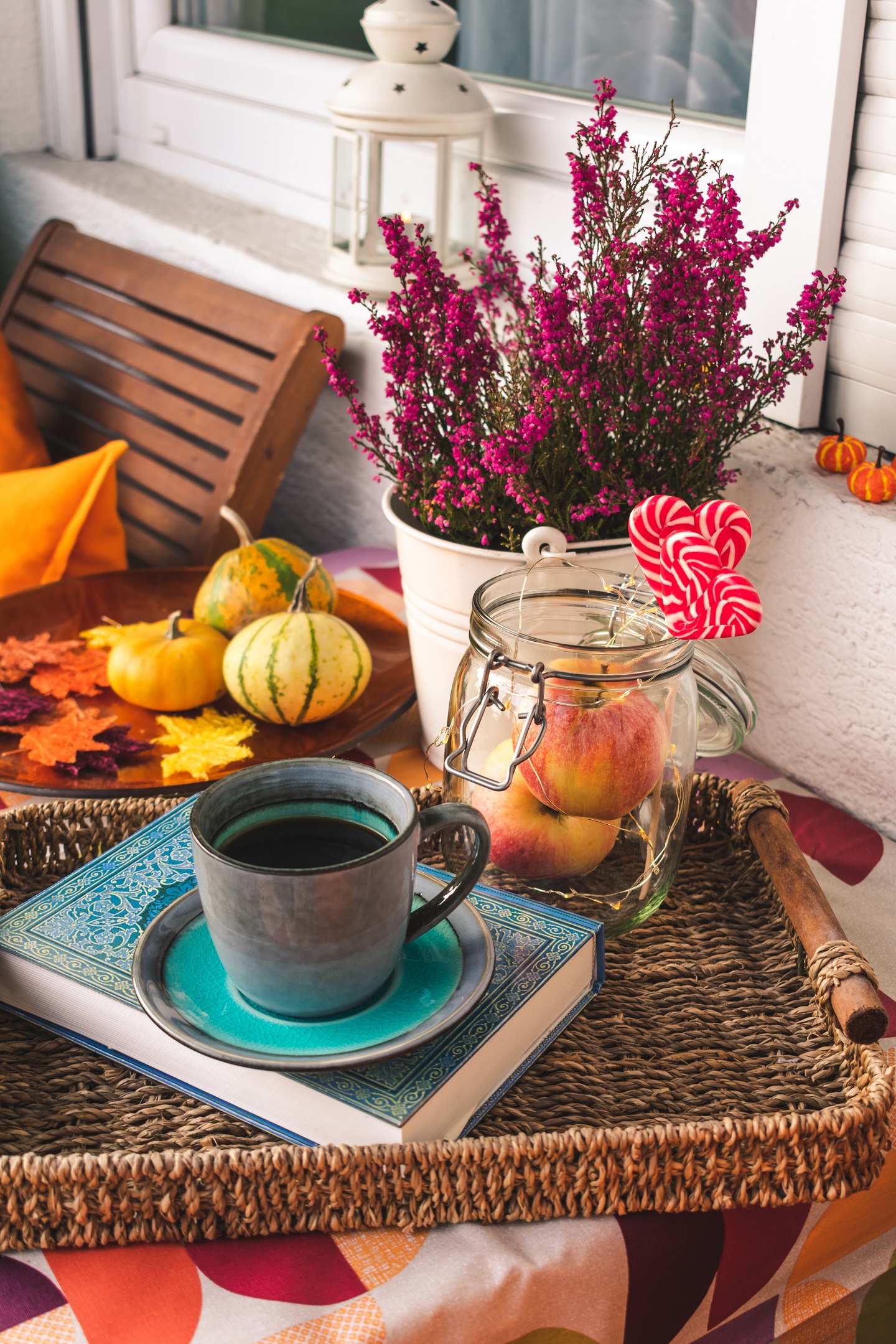 Herbstlich dekorierter Balkon mit Kürbissen, bunten Blättern, Tee und einem Buch auf dem Tisch